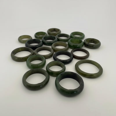A group of twelve polished stone rings in earthy green, brown, and dark marbled tones, arranged on a plain light background.