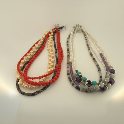 Two beaded necklace strands displayed on a white surface. The left necklace features red, cream, and dark brown beads.