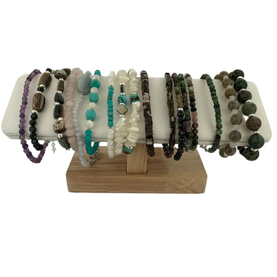 A variety of beaded bracelets displayed on a white stand with a wooden base, set against a plain white background.